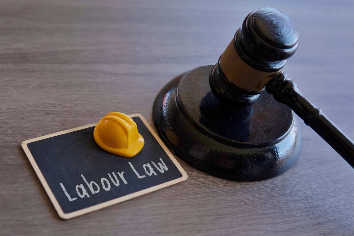 Closeup image of yellow hard hat and judge gavel. Labour law concept.