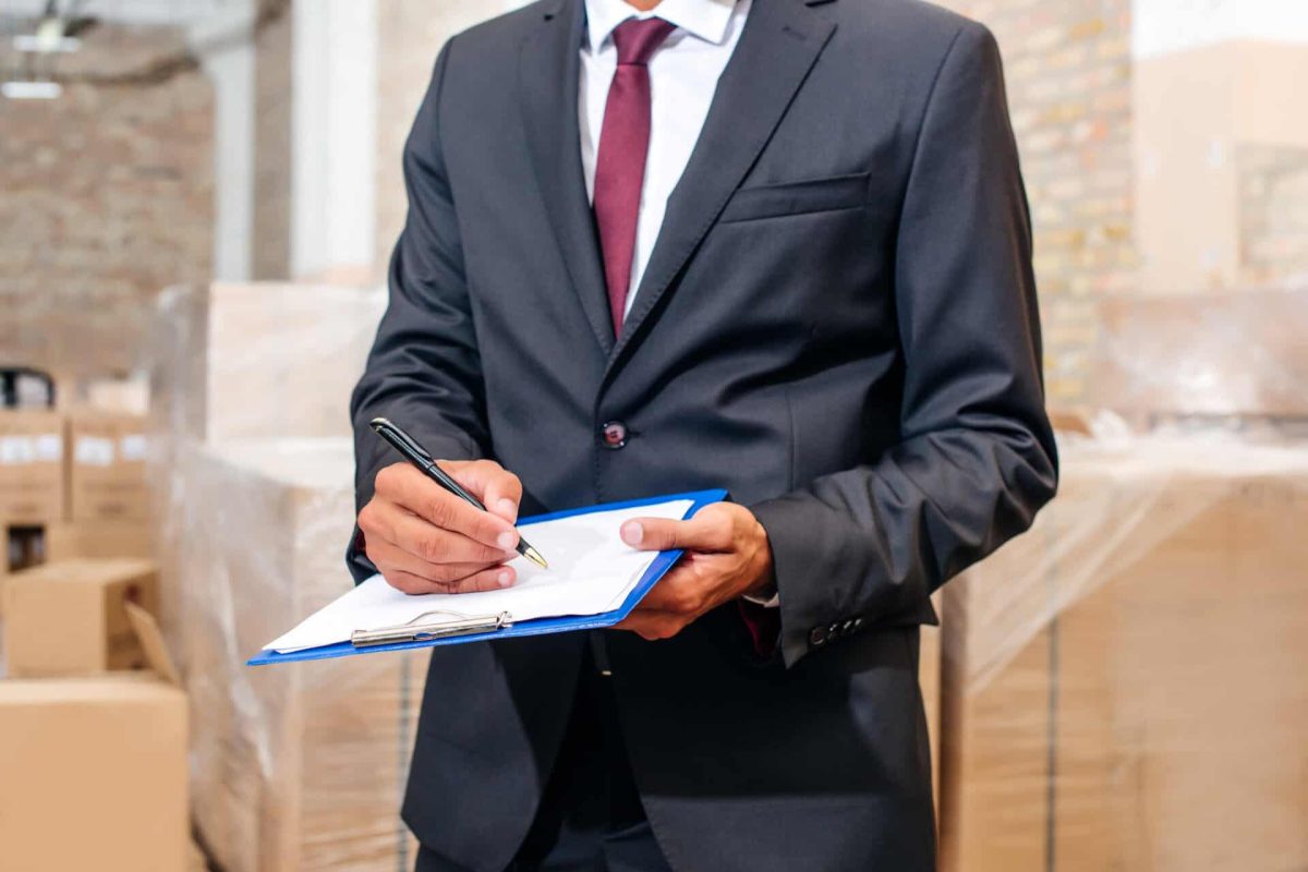 cropped shot of businessman writing on clipboard at warehouse