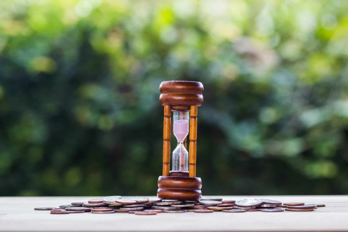 Money savings, Investment, time and money growing concept : hourglass on stack coins on with blurred nature background on wooden table. Saves money for the future. Time investment use money for work.