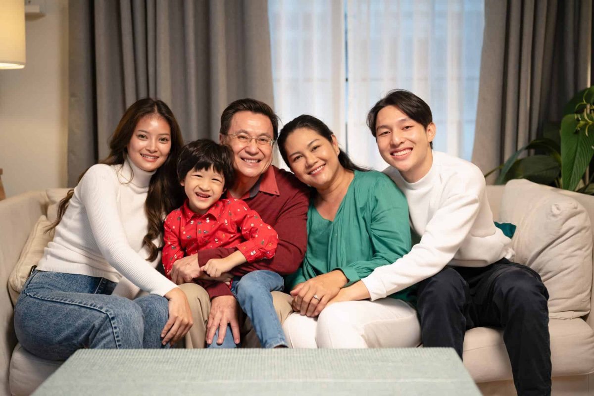 Portrait of Asian parents, child, and grandparents sitting on the sofa in the living room at home.