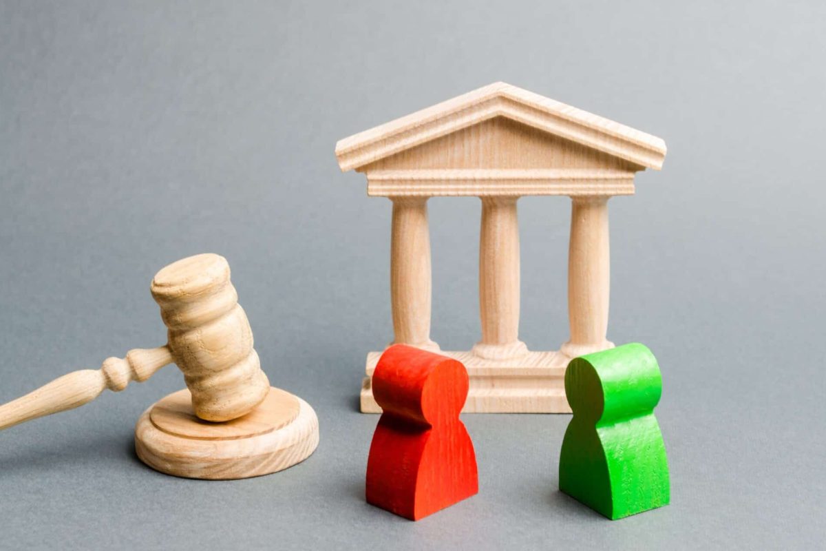 Wooden figures of people standing near the judge's gavel. Litigation. Business rivals. Conflict of interest. Law and justice. The layer's services. Two opponents. Judgment. Gavel. Red and green